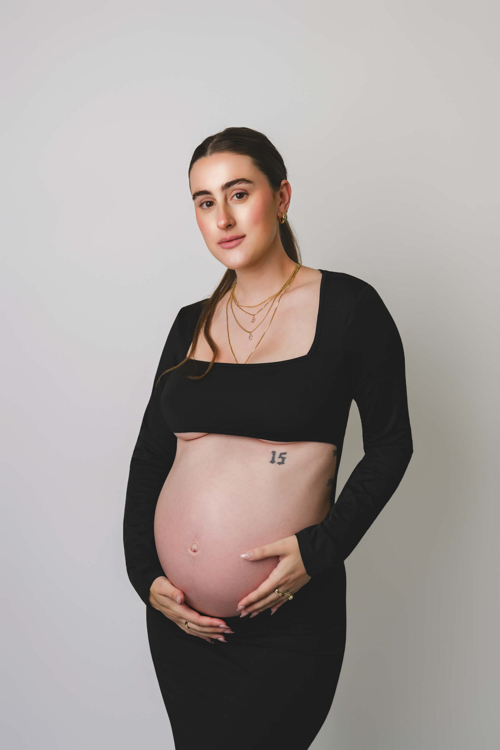 A pregnant woman in a black top and skirt holds her hands on her bump with a smile after exploring baby shower venues in san francisco