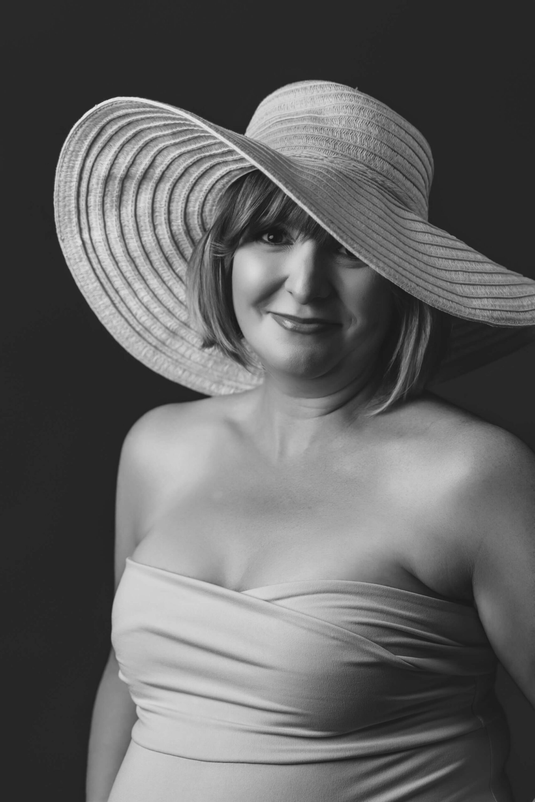 a pregnant woman smiles in a studio wearing a large brim hat