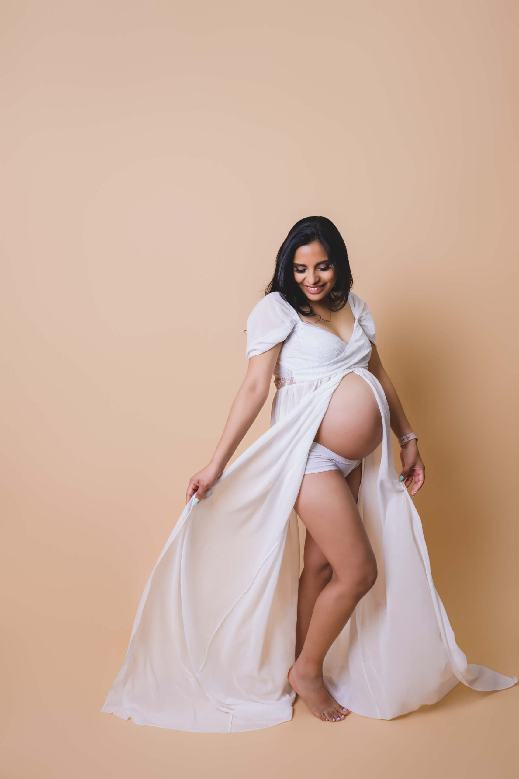 a giggling mother to be twirls in her open white maternity gown in a studio after finding doulas in marin