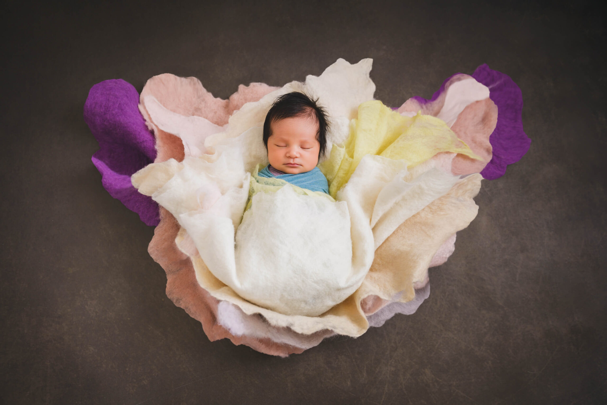 A sleeping newborn in a blue swaddle wrapped in colorful cloths in a studio after meeting lactation consultants in san francisco