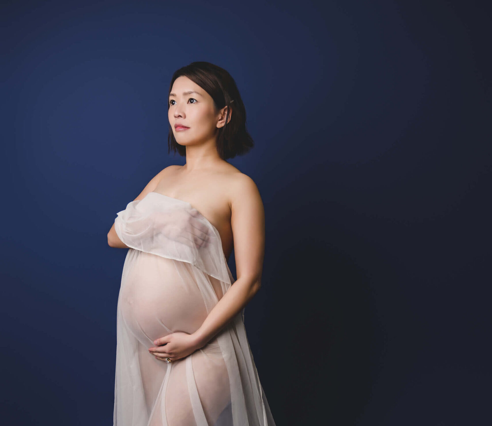 A mother to be wrapped in a sheer silk stands in a studio with a hand under her bump after meeting with midwives in san francisco