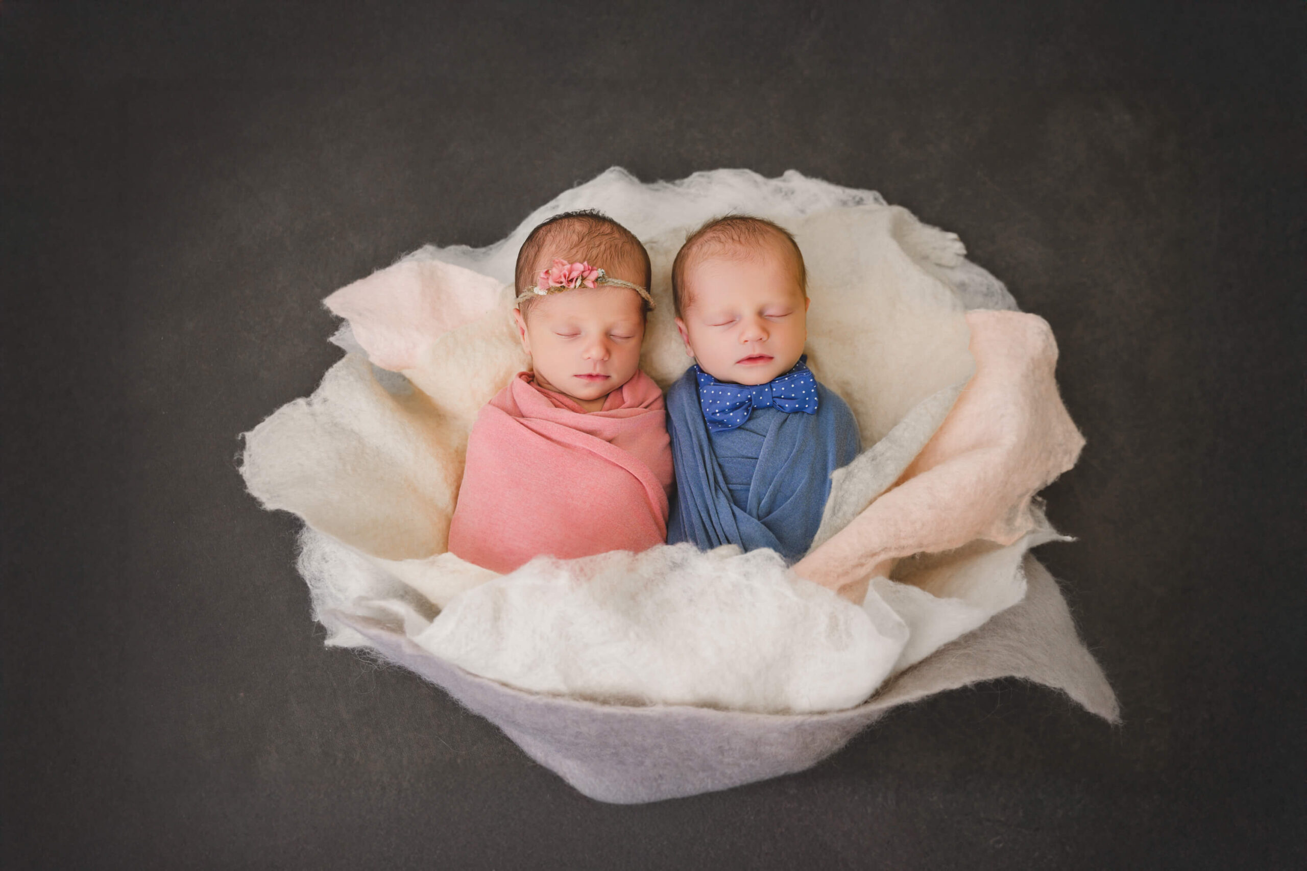 Sleeping newborn baby twins in pink and blue swaddles lay together in a felt bowl in a studio after meeting postpartum doulas in san francisco